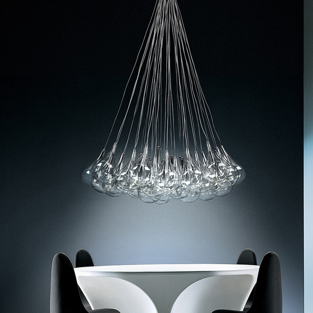 Yarvelle 37 Light Glass Pendant Light in chrome, a cluster of clear teardrop glass globes on fine cables gathered to a single point, shown above a white table in a dark room.