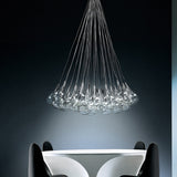 Yarvelle 37 Light Glass Pendant Light in chrome, a cluster of clear teardrop glass globes on fine cables gathered to a single point, shown above a white table in a dark room.