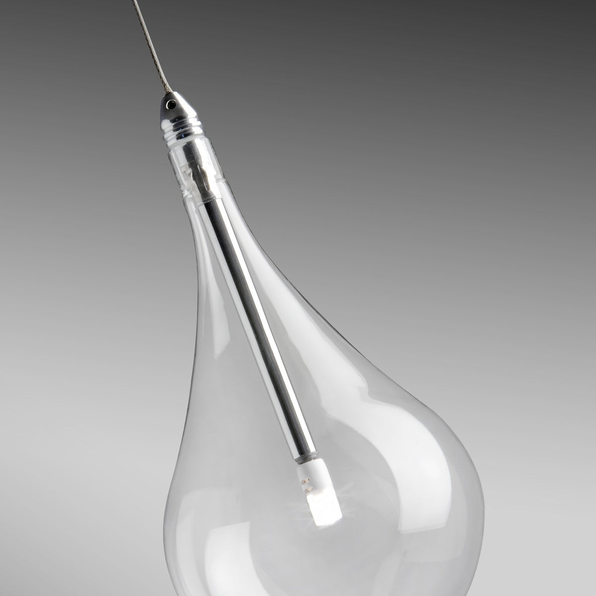 Close-up of a Yarvelle pendant light glass teardrop globe with chrome holder and LED chip inside, suspended on a fine cable against a grey background.