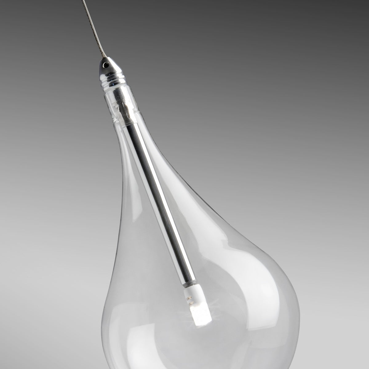 Close-up of a Yarvelle teardrop glass pendant shade with slim chrome stem and small internal LED lamp, suspended on a cable against a grey background.