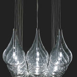 Yarvelle 24 Light Glass Pendant Light in chrome, close-up of teardrop-shaped glass shades with slim chrome stems and lit G4 lamps, set against a dark background.