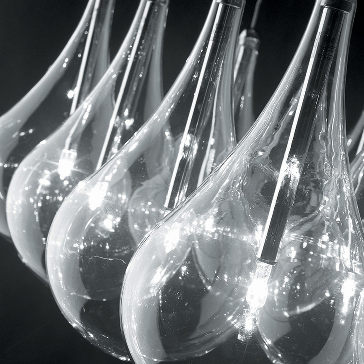 Yarvelle 24 Light Glass Pendant Light in chrome, close-up of clear teardrop glass shades with slim chrome stems and illuminated G4 lamps, set against a dark background.