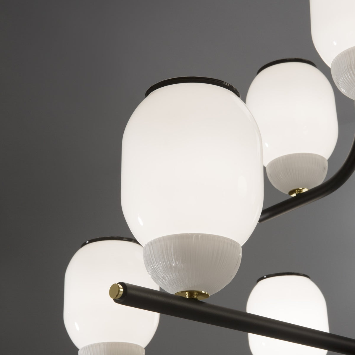 Close-up of the Faronne 9 Light Glass Chandelier in black, showing white opal glass barrel shades with ribbed bases on black iron arms with brass fittings.