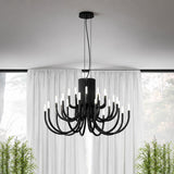 ThePalm LED 18 Light Chandelier in black, with curved arms in two tiers rising from a fluted column, hung above sheer curtains in a living room setting.