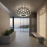 A modern hallway with concrete walls and floors showcases the Mesh LED Flush Ceiling Light in black, a built-in planter with succulents, a minimalist bench, and large glass doors that overlook a pool and rocky landscape.