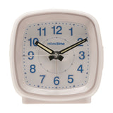 White square cushion alarm clock with rounded corners, plastic case, white dial, blue Arabic numerals, and black luminous hour and minute hands.