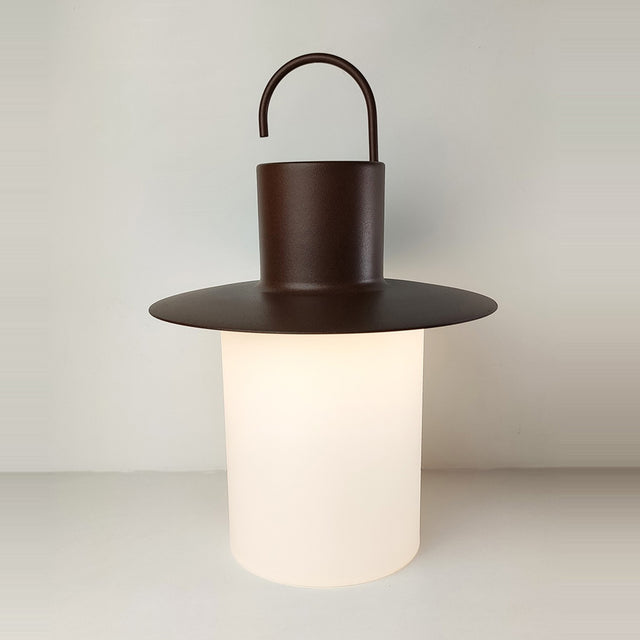 Nautic LED rechargeable outdoor table lamp in Corten rust finish, lantern shape with hook handle, wide flat brim, and glowing opal cylinder, on a plain light background.