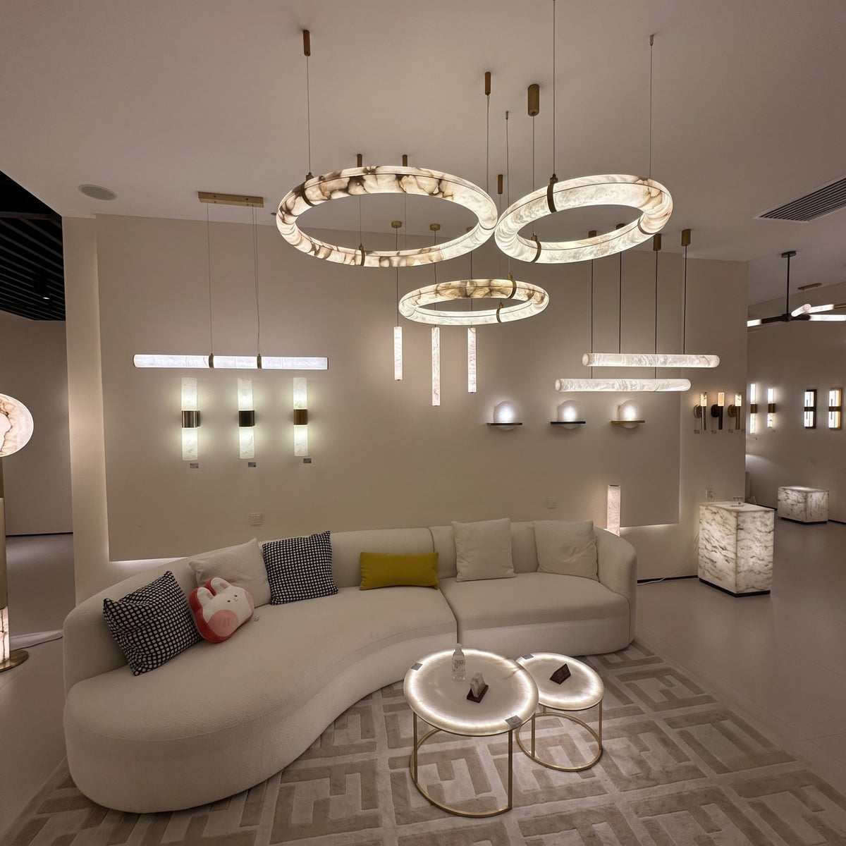 Aureon LED Triple Ring Alabaster Chandelier in brushed brass, three staggered circular rings glowing warm white above a living room seating area.