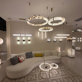 Aureon LED Triple Ring Alabaster Chandelier in brushed brass, three staggered circular rings glowing warm white above a living room seating area.