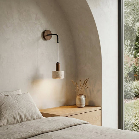 Minimalist bedroom with light beige bedding, a wooden nightstand holding a vase of dried grasses, the Torvella 1 Light Hanging Drum Travertine Wall Light in walnut brown & light beige, an arched alcove, and large window revealing greenery.