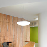 Stone LED Pendant Light in white, a broad flat oval shade suspended on slim wires, shown illuminated above a reception desk in a wood-panelled interior.