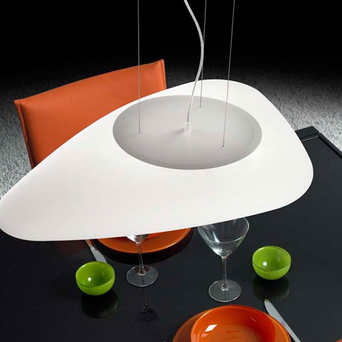 Stone LED Pendant Light in white, a flat pebble-shaped asymmetric shade hung above a glass dining table set with an orange chair and green bowls.