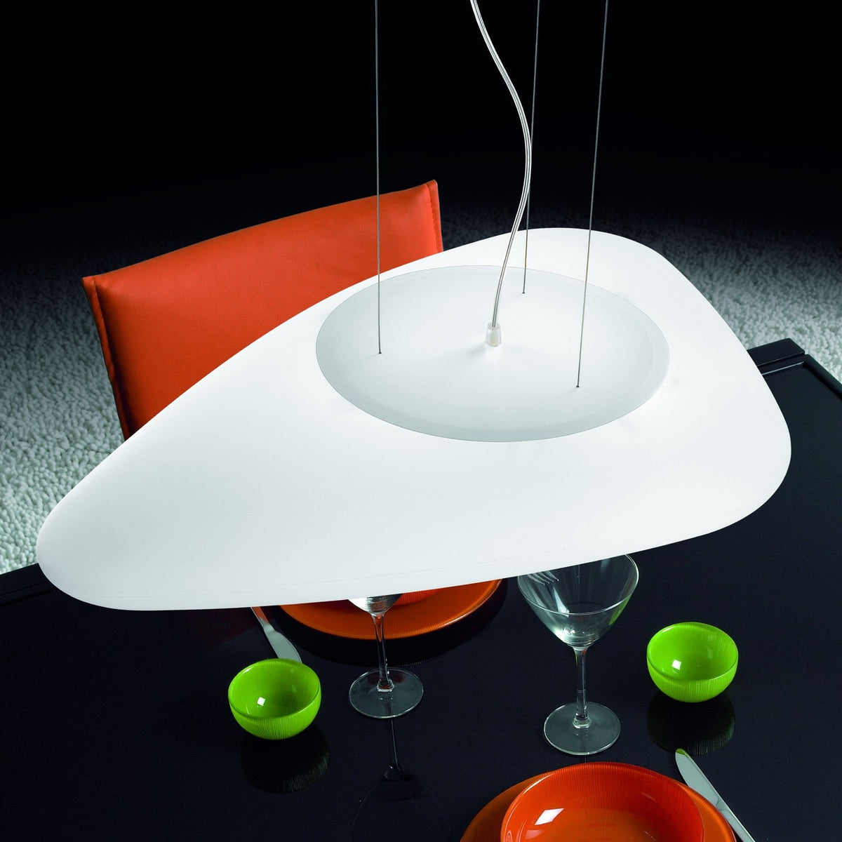 Stone LED Pendant Light in white, a flat pebble-shaped shade suspended on fine wires above a glass dining table with an orange chair in a dining room setting.