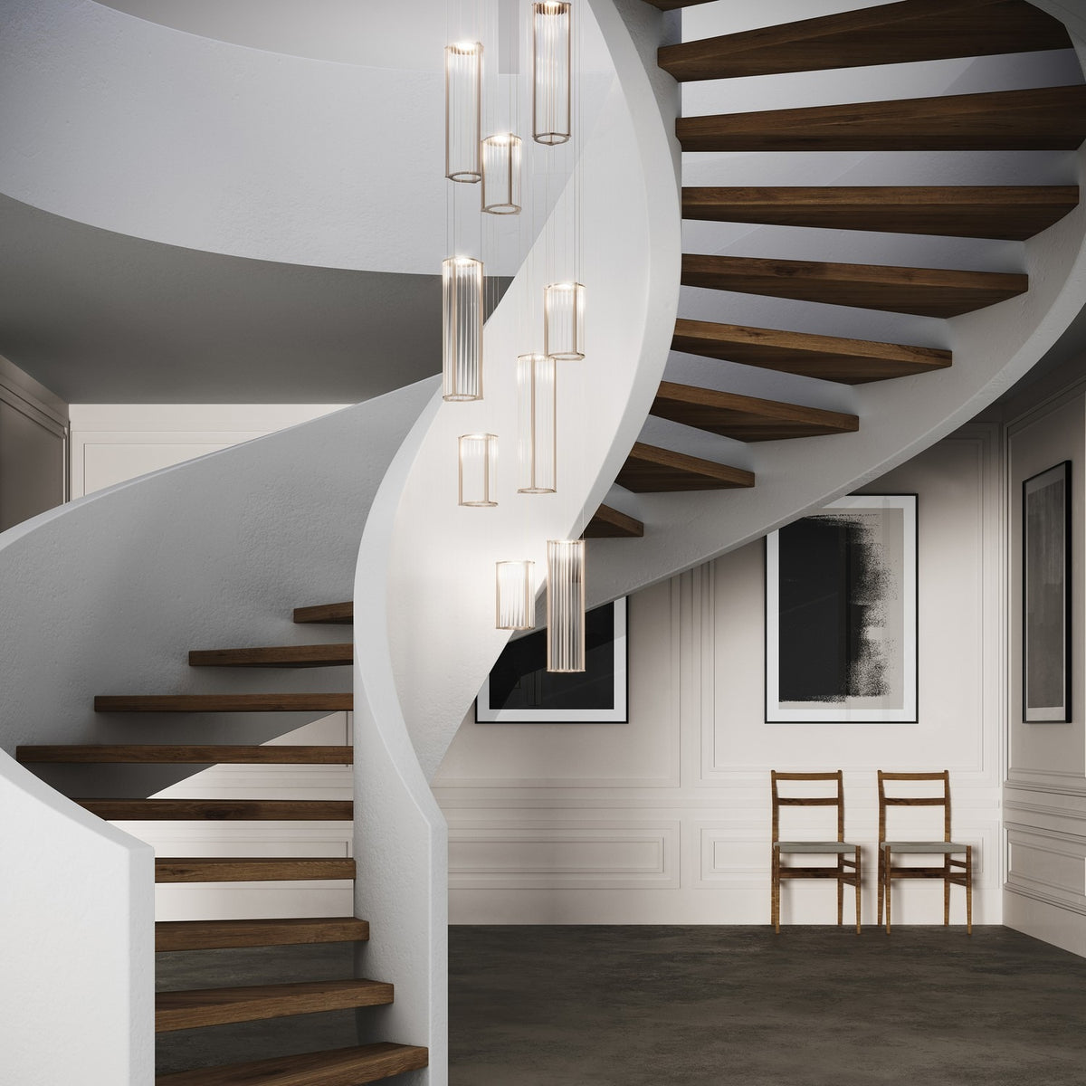 Kalvenne LED glass pendant lights in satin bronze with ribbed glass columns and iron frames, shown as a multi-light cluster above a spiral staircase.