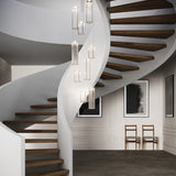 Kalvenne LED glass pendant lights in satin bronze with ribbed glass columns and iron frames, shown as a multi-light cluster above a spiral staircase.