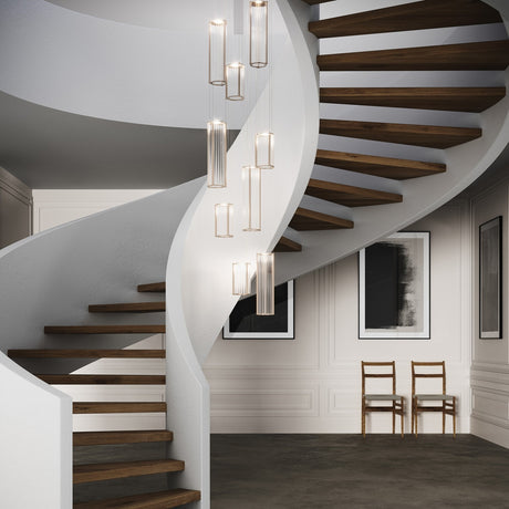 Kalvenne LED glass pendant lights in satin bronze with ribbed glass columns and iron frames, shown as a multi-light cluster above a spiral staircase.