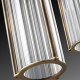 Close-up of the Kalvenne LED glass pendant light with ribbed glass columns in a satin bronze iron frame, shown against a dark gradient background.
