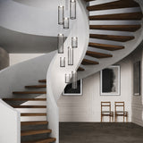 Kalvenne LED glass pendant lights in black, shown as multiple ribbed glass columns in fine black iron frames cascading beside a spiral staircase with wood treads.
