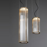 Kalvenne LED glass pendant light in satin bronze, two cylindrical fixtures with ribbed glass columns in iron frames, suspended on thin cables against a grey background.