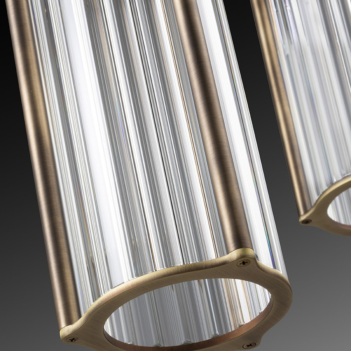 Close-up of the Kalvenne LED glass pendant light, showing ribbed clear glass cylinders in satin bronze iron frames with visible screw fittings, set against a dark gradient background.