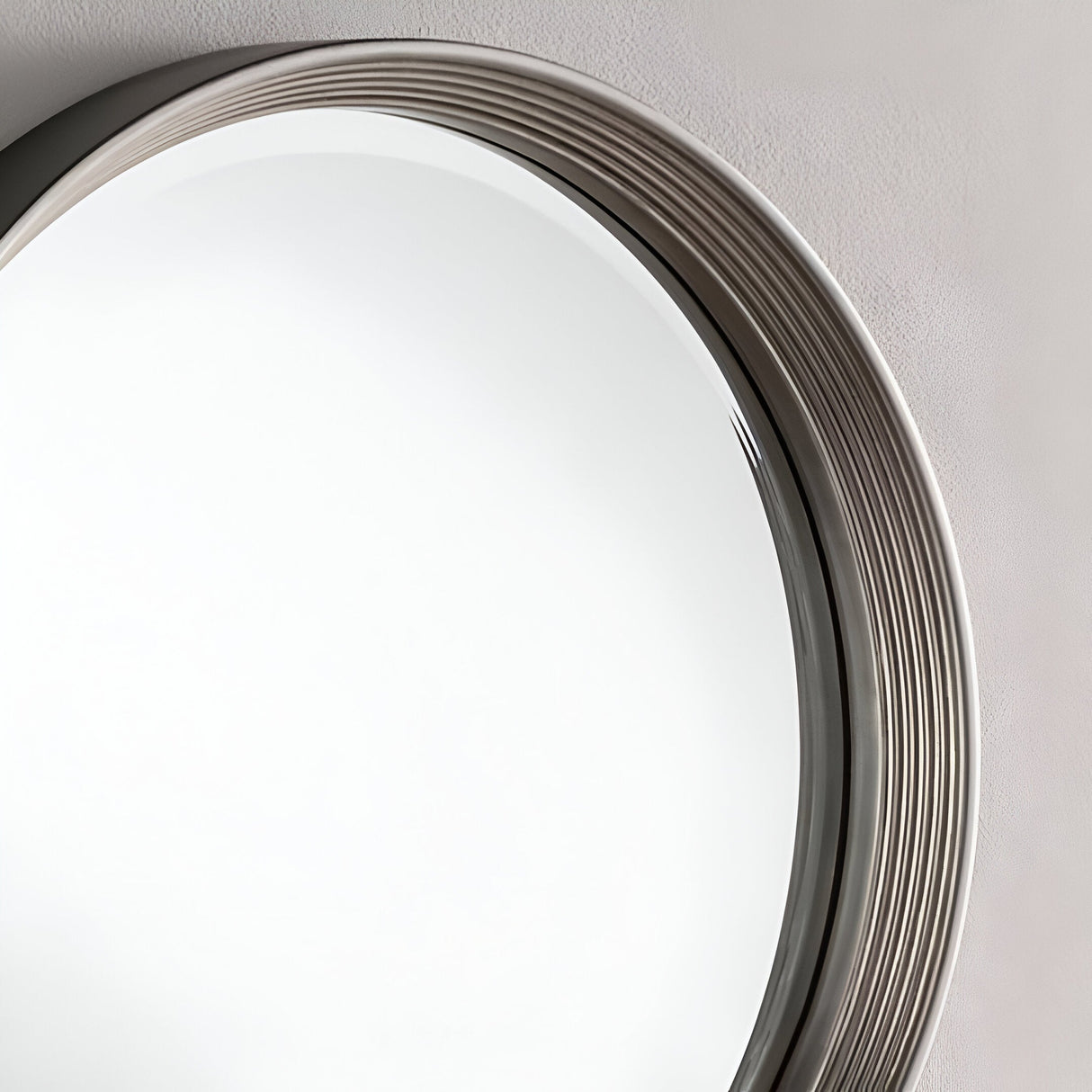 A close-up of the Solune Circle Wall Mirror Black & Silver - 61cm on a wall highlights its thick, ridged frame with a metallic finish. The mirrors reflective surface contrasts with the smooth, neutrally painted wall, showcasing its contemporary design and modern aesthetics.
