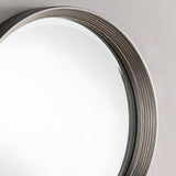 A close-up of the Solune Circle Wall Mirror Black & Silver - 61cm on a wall highlights its thick, ridged frame with a metallic finish. The mirrors reflective surface contrasts with the smooth, neutrally painted wall, showcasing its contemporary design and modern aesthetics.