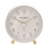 Round white alarm clock with matt metal case, gold feet, and gold hour, minute, and second hands on a clear Arabic numeral dial, shown on a plain background.