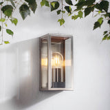 Endon Castwick silver box lantern wall light with bevelled glass panels and E27 filament bulb, mounted on a white wall beneath green foliage.