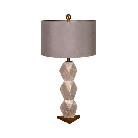 The Zerava 1 Light Faceted Marble Table Lamp features a black and grey three-section faceted base, a wide round grey fabric shade, and a small gold finial, creating a modern sculptural look.