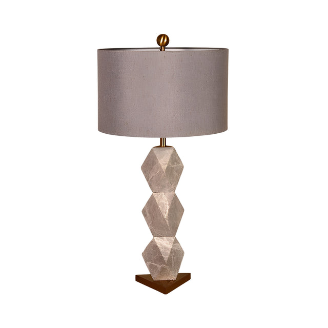 The Zerava 1 Light Faceted Marble Table Lamp features a black and grey three-section faceted base, a wide round grey fabric shade, and a small gold finial, creating a modern sculptural look.