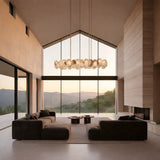 Niori Solvane linear chandelier with a row of alabaster petals on a slim brass bar, suspended in a vaulted living room with mountain views.