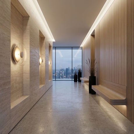 A modern hallway with light wood and beige stone walls, built-in benches, potted plants, a large window showing a dusk city skyline, and gold Blossom LED Glass Wall Lights for elegant illumination.