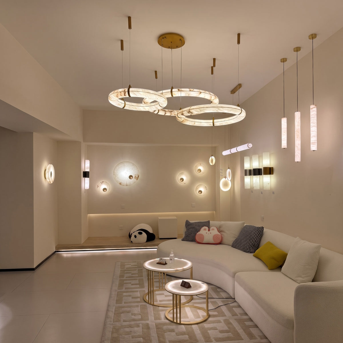 Aureon LED Triple Ring Alabaster Chandelier in brushed brass, three staggered circular rings suspended over a living room seating area with warm ambient glow.