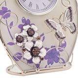 Close-up of a purple oval glass mantel clock featuring frosted floral glass, a raised silver and white butterfly, and crystal-centred white flowers on a silver base.