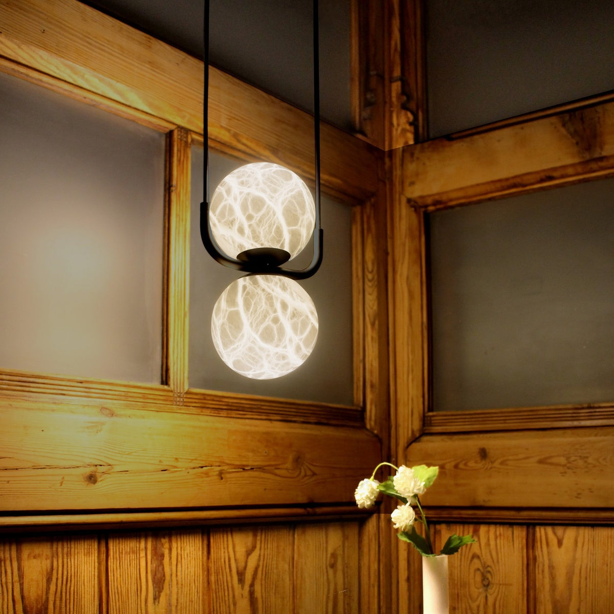 Halvessa LED 2 Light Alabaster Dimmable Pendant Light in black, two glowing marbled globes on a U-shaped bracket with twin cables, shown against wood-panelled walls.