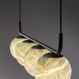 Halvessa LED 4 Light Alabaster Dimmable Pendant Light in black, close-up of glowing alabaster globes with veining beneath a slim angled iron bar, grey background.