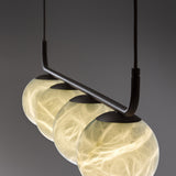 Halvessa LED 4 Light Alabaster Pendant Light in black, close-up of four glowing globes with veined texture suspended from a slim angled black bar, shown against a grey background.