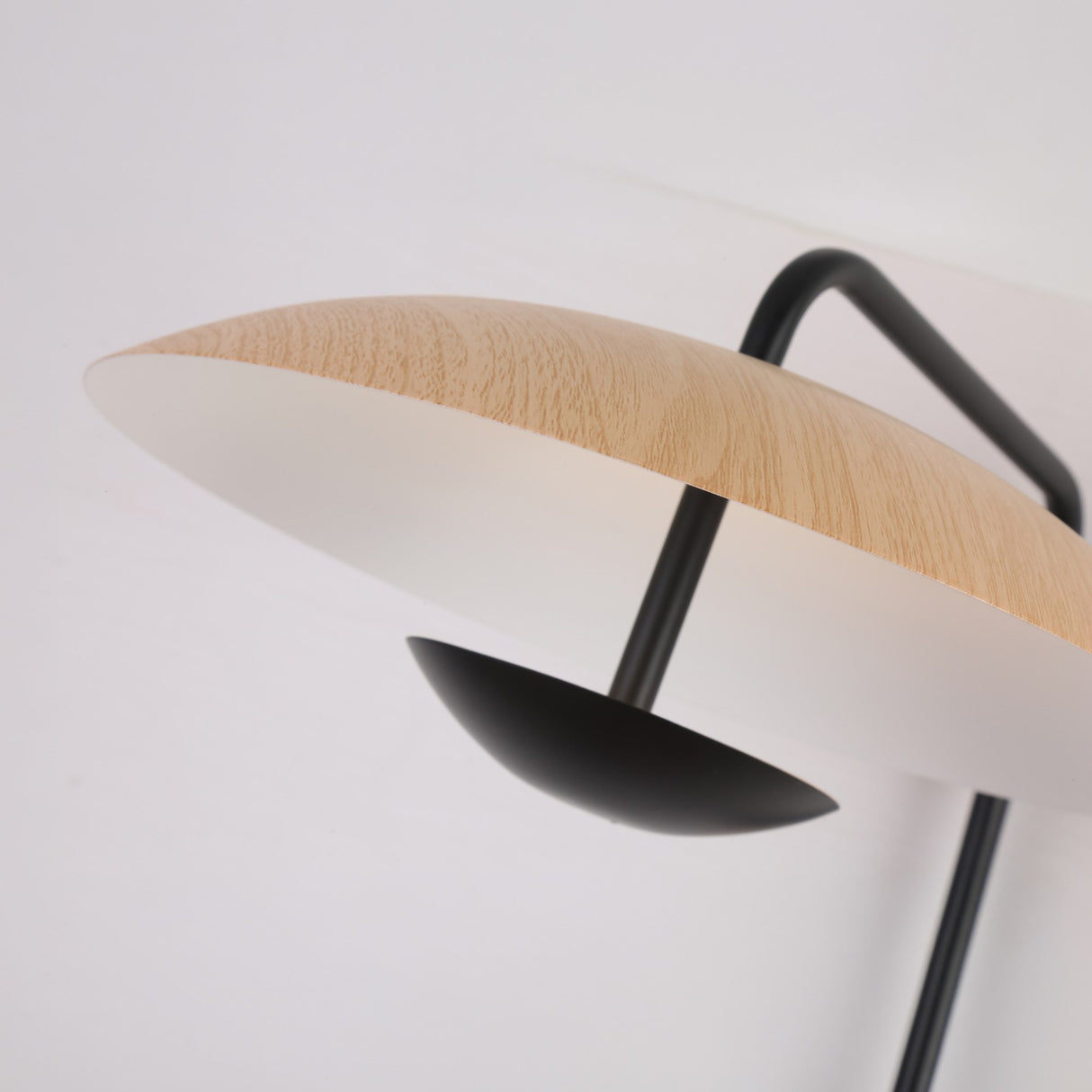 Close-up of Niori Ginger LED Wall Light showing a wood-grain disc shade above a small black bowl reflector on a curved black metal arm.