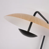 Close-up of Niori Ginger LED Wall Light showing a wood-grain disc shade above a small black bowl reflector on a curved black metal arm.