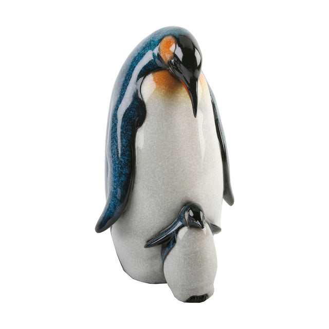 Resin figurine of an adult penguin bowing its head over a chick, white body with mottled blue wings, glossy black heads and orange neck patches, high-gloss finish on a plain white background.
