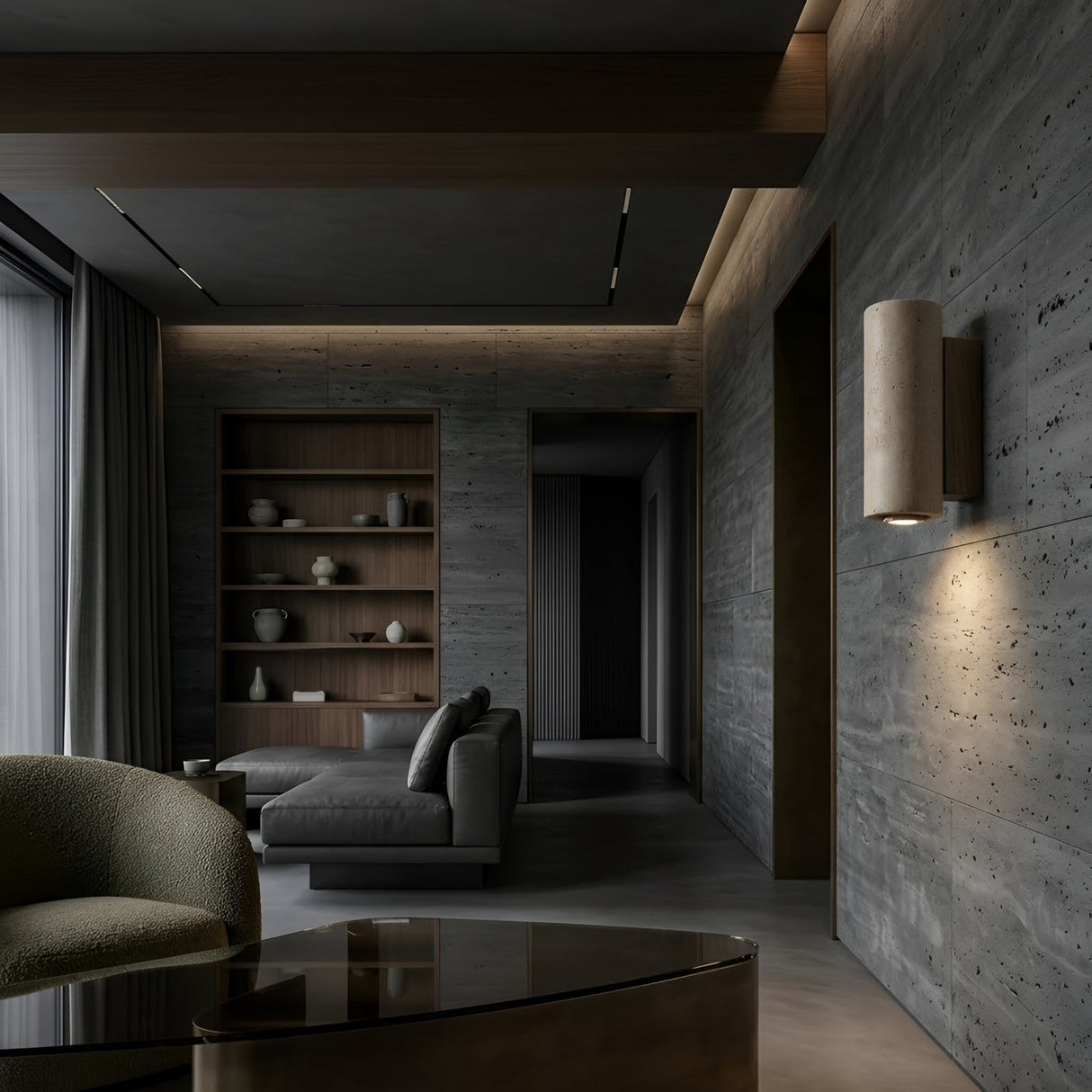 A modern living room with gray textured walls, walnut brown built-in shelves, a gray sectional, floor-to-ceiling curtains, and the Dorsa 1 Light Small Cylinder Travertine Wall Light in Walnut Brown & Light Beige for a minimalist touch.