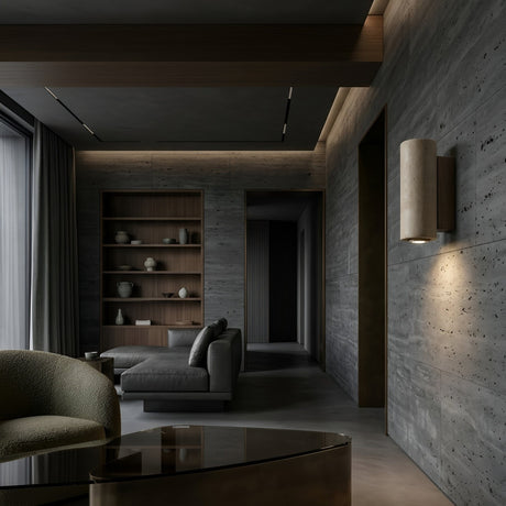 A modern living room with gray textured walls, walnut brown built-in shelves, a gray sectional, floor-to-ceiling curtains, and the Dorsa 1 Light Small Cylinder Travertine Wall Light in Walnut Brown & Light Beige for a minimalist touch.