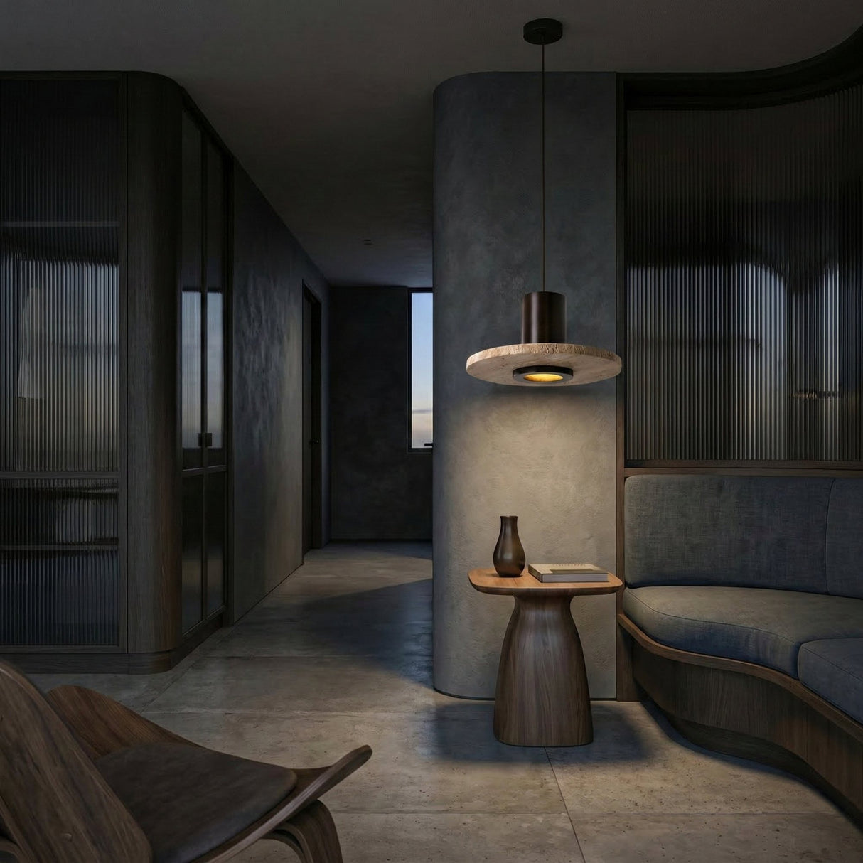 A modern, dimly lit living space features a curved sofa, wooden side table with a vase and book, and the Torvane 1 Light Medium Wide Disc Travertine Single Pendant Light in Walnut Brown & Light Beige overhead. Textured gray walls and floors complete the look.