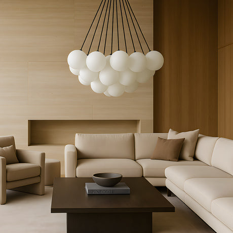 A modern living room with beige sofas, a matching armchair, a dark wood coffee table with books and a bowl, and the Orb 17 Light Cluster Suspension - Black as an eye-catching chandelier. Warm neutral wood tones accent the walls and decor.