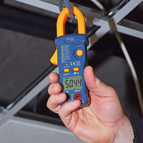 Hand holding the Mercury CMTS01 Smart Digital Clamp Multimeter in blue and yellow, LCD showing 50.44 Hz, with COM and INPUT ports below.