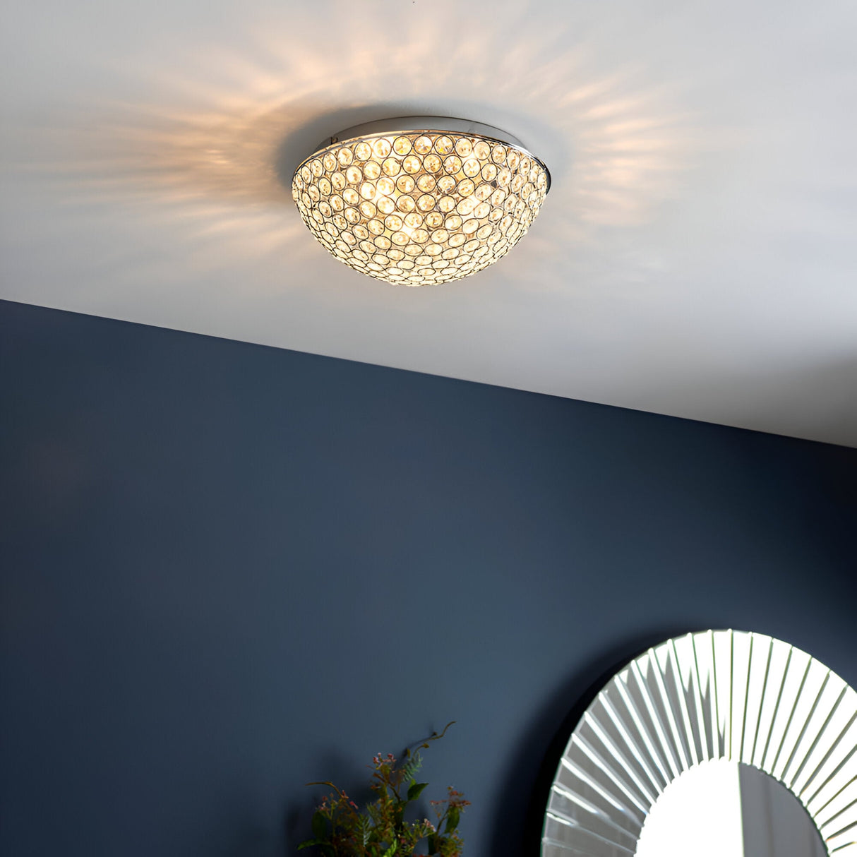 Endon Cordelia 3 light crystal flush bathroom ceiling light in chrome, illuminated on a white ceiling above a deep blue wall with a sunburst mirror.