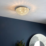 Endon Cordelia 3 light crystal flush bathroom ceiling light in chrome, illuminated on a white ceiling above a deep blue wall with a sunburst mirror.