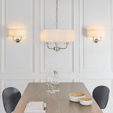 Endon Castdon 3 light pendant in nickel with white drum shade, flanked by matching twin wall lights above a dining table in a panelled room.