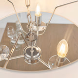 Close-up of Endon Castdon 3 light pendant in nickel with lit E14 candle bulbs, K9 crystal bobeches, chain suspension and mirrored disc above a dining table.
