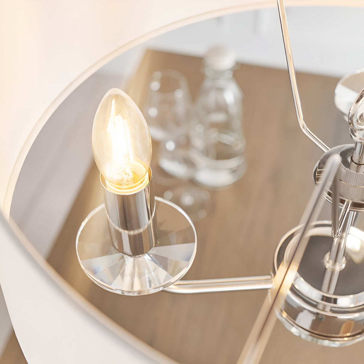 Close-up of Endon Castdon 3 Light Pendant in nickel with K9 crystal bobeche, E14 candle bulb and white faux silk shade above a dining table.